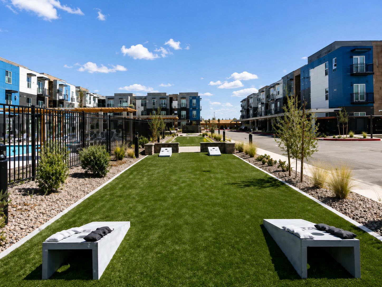 A residential complex with a central lawn, outdoor seating areas, and modern apartment buildings.