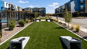Um complexo residencial com gramado central, áreas de estar ao ar livre e edifícios de apartamentos modernos.