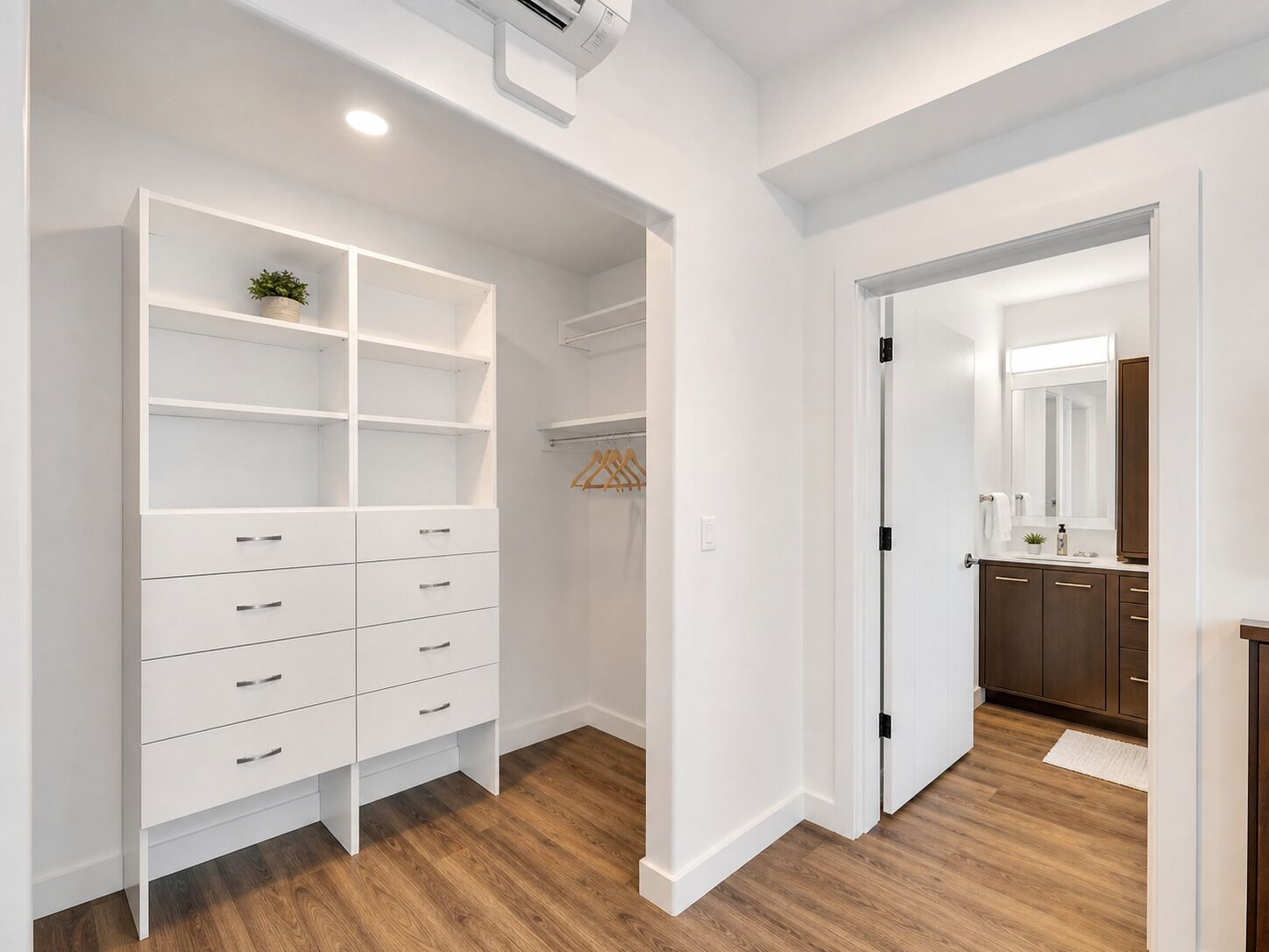 A walk-in closet with open shelving, a hanging rod, and a door leading to a bathroom with a mirror and sink.
