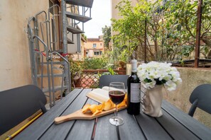 Area pranzo all'aperto con tavolo apparecchiato per due, bottiglia di vino, un bicchiere e un piatto di patatine.