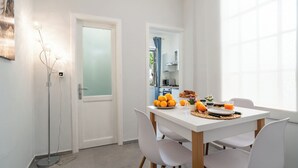 Un coin repas avec une table blanche, quatre chaises et une vue sur la cuisine grâce à une porte ouverte.