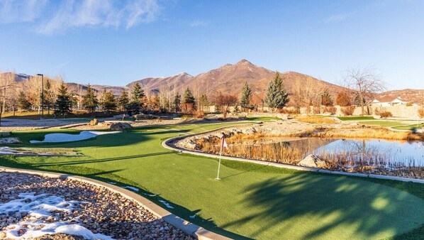 A golf course with a flag, a pond, and mountains in the background.