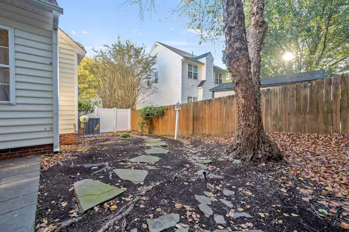 A backyard with a stone pathway, a wooden fence, and a tree.