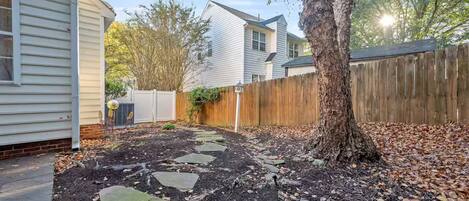 A backyard with a stone pathway, a wooden fence, and a tree.