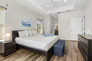 Ein Schlafzimmer mit einem Bett, Nachttischen, einer Bank, einem Deckenventilator und einer Tür zu einem anderen Raum.