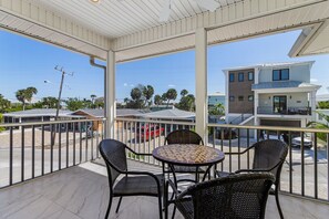 Ein Balkon mit Korbstühlen und einem runden Tisch, mit Blick auf eine Straße mit parkenden Autos und Gebäuden.