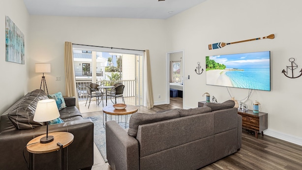 A modern living room with a sofa, a coffee table, and a TV. There is a balcony with a view of the sea. - Private Heated Pool | Spacious 3BR House (Fort Myers Beach)