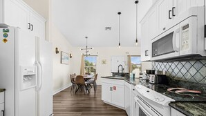 A modern kitchen with white cabinets, a built-in oven, a microwave, and a dining area with a table and chairs. - Private Heated Pool | Spacious 3BR House (Fort Myers Beach)