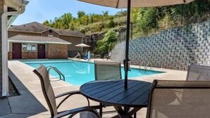 A swimming pool with lounge chairs and an umbrella, surrounded by a brick wall and a hillside.