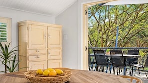 Un coin repas avec une table ronde en bois, un panier en osier rempli de citrons et une vue sur l’espace extérieur aménagé, visible à travers une porte vitrée.