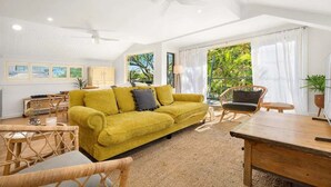 Un salon spacieux avec un canapé jaune, des meubles en osier et un ventilateur de plafond.