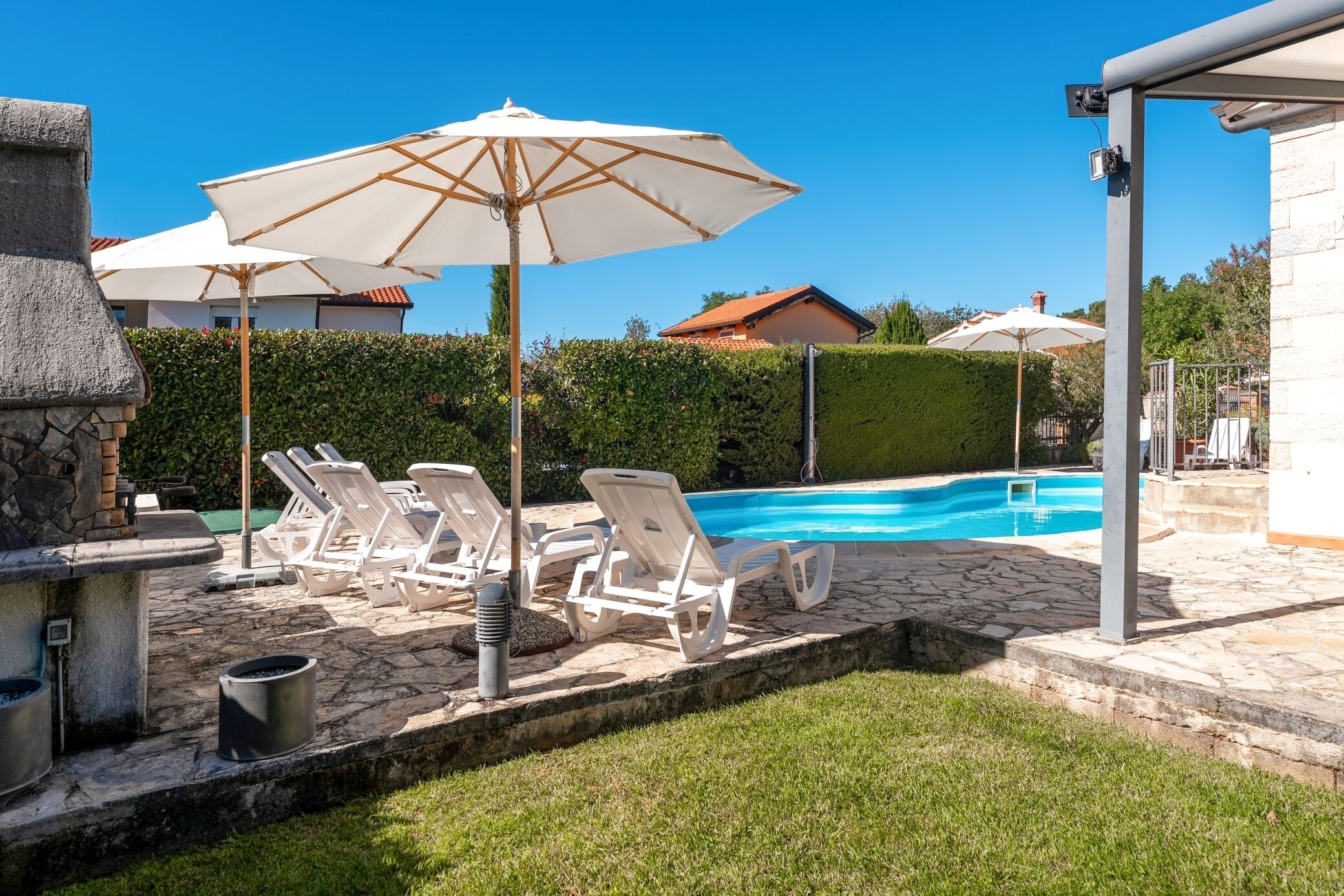 Ein Poolbereich mit Liegestühlen und Sonnenschirmen, Steinboden und einer Steinwand.
