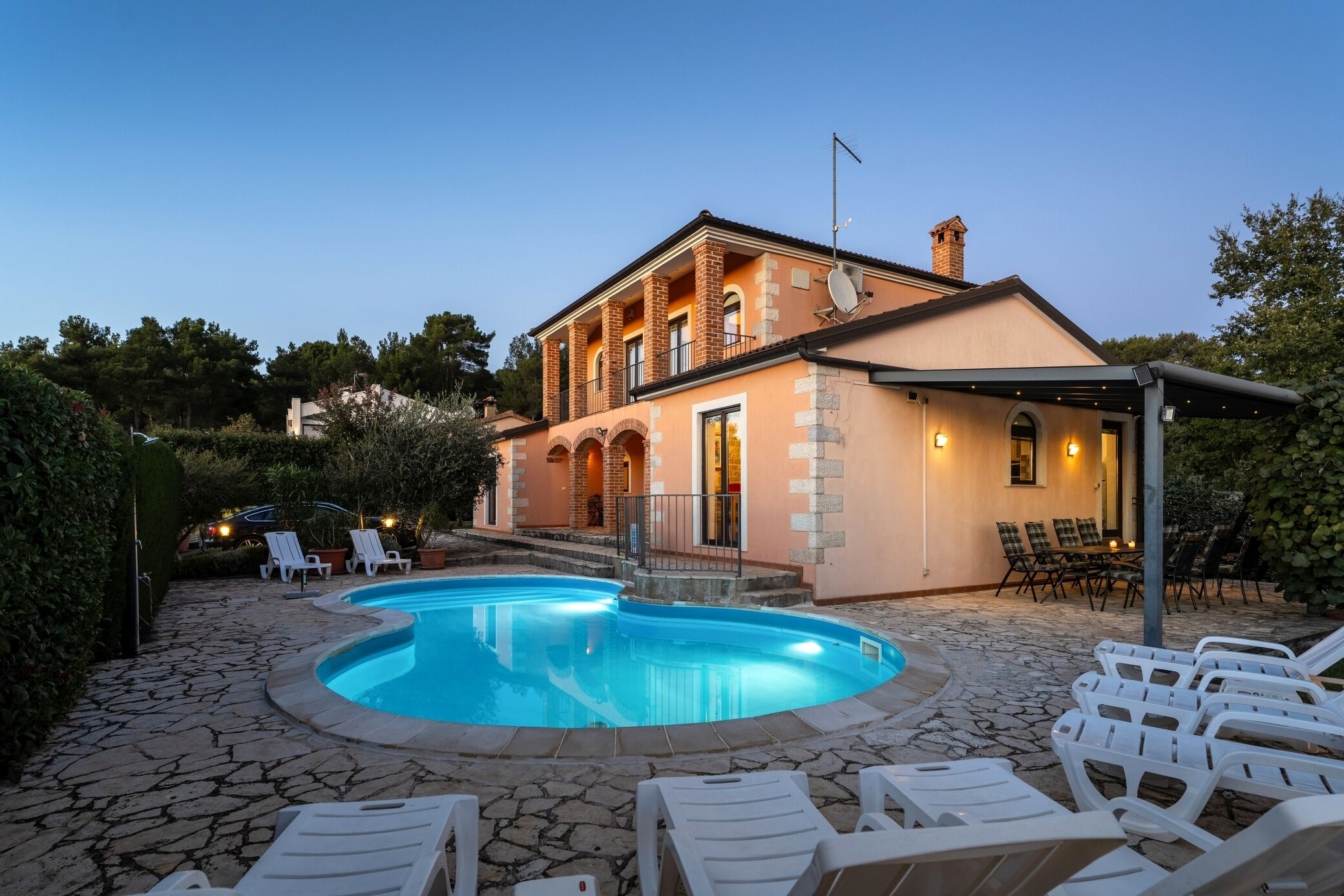Ein zweistöckiges Haus mit Swimmingpool, Sitzgelegenheiten im Freien und einer Steinterrasse.