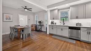 Une cuisine moderne avec des meubles gris, un lave-vaisselle en acier inoxydable et un coin repas comprenant une table en bois et des chaises grises.