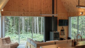 A modern kitchen with a large island, a built-in stove, and a view of the forest through large windows. - Chalet Saison | Nature • Sauna - Hiking - Softness (Chertsey)