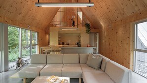 A modern interior with a large sectional sofa, a dining area, and a kitchen. - Chalet Saison | Nature • Sauna - Hiking - Softness (Chertsey)