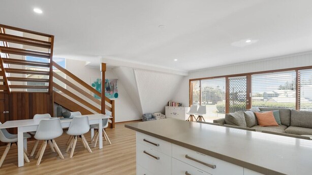 Una cocina moderna con comedor, una escalera de madera y un ventanal con persianas.