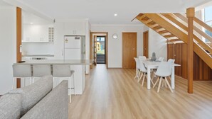 Una cocina moderna con armarios blancos, horno empotrado y comedor con escalera de madera.