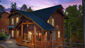 A log cabin with a porch, stone accents, and a metal roof.