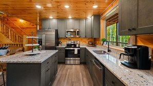 A modern kitchen with granite countertops, stainless steel appliances, and a wooden ceiling.