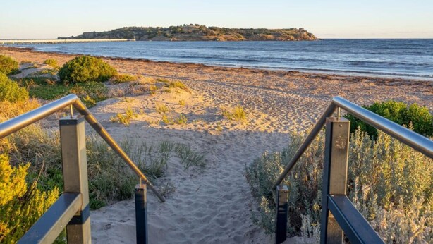 Een strandpad dat naar de zee leidt, met een eiland in de verte.