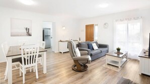 Een moderne woonkamer met een eetgedeelte, een grijze bank en een houten eettafel.