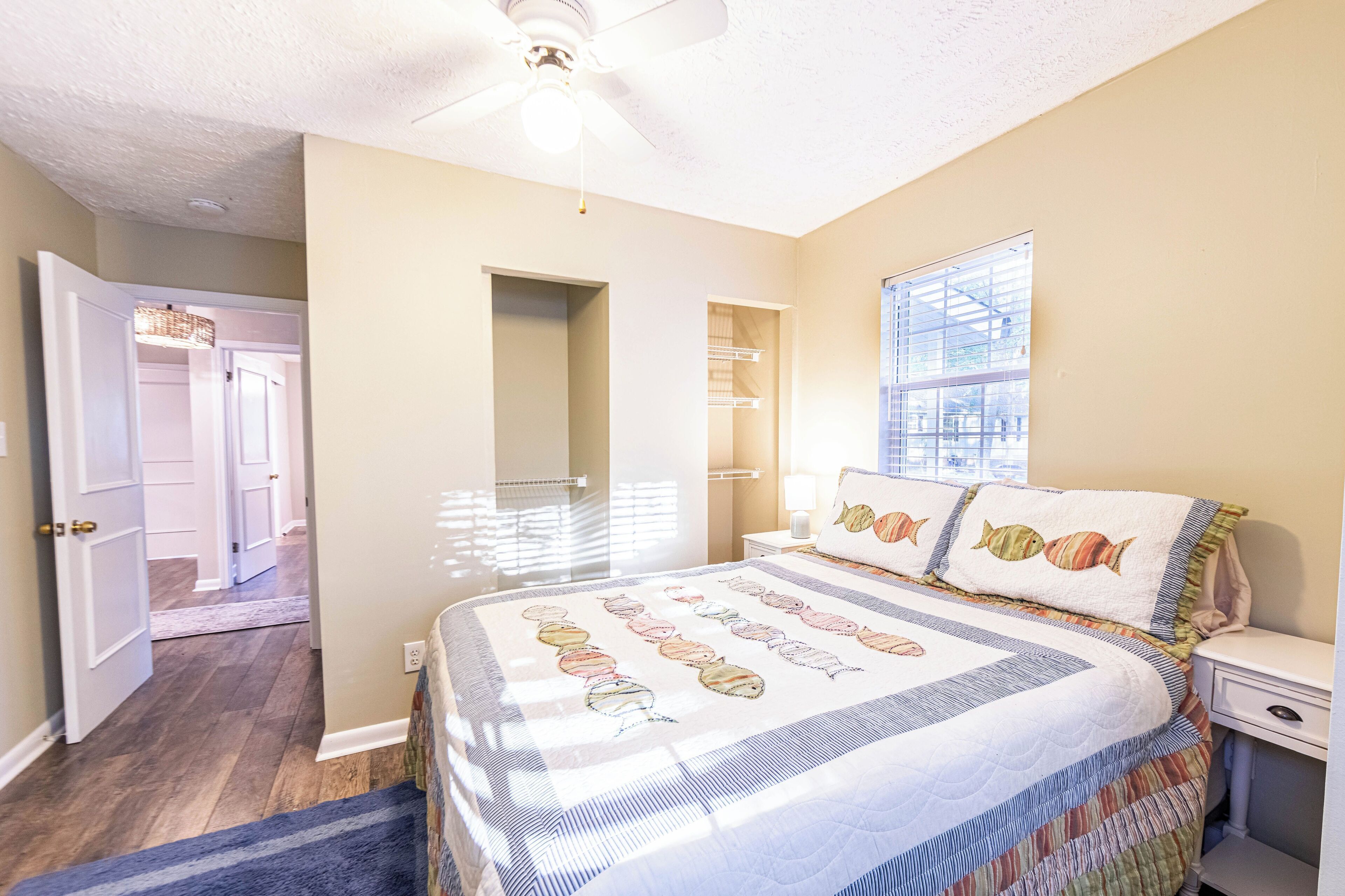 Un dormitorio con cama, mesita de noche, ventana y puerta que da a otra habitación.