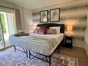 Une chambre à coucher avec un lit, des tables de chevet, une fenêtre et une vue sur la verdure.