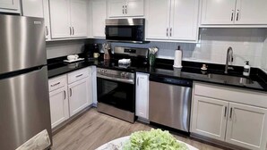 Una cocina moderna con electrodomésticos de acero inoxidable, armarios blancos y encimera negra.