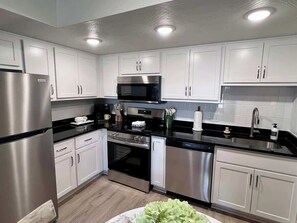 A modern kitchen with stainless steel appliances, white cabinetry, and a black countertop.