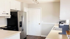 A modern kitchen with white cabinetry, a stainless steel refrigerator, a black stove, and a white door. - Dothan Westside Retreat (Dothan)