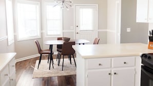 A modern kitchen with white cabinetry, a central island, and a dining area with a round table and chairs. - Dothan Westside Retreat (Dothan)