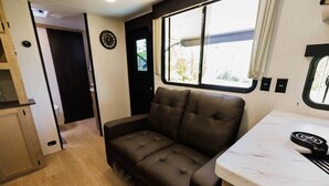 A compact RV interior with a sofa, a small kitchen area, and a window providing natural light. - New 2026 RV / Mountain View / ATVs (Lincoln)