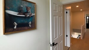 Ein Flur mit einer zur Toilette führenden Tür, einem Gemälde, das einen Leopard in einer Badewanne zeigt, und einer im Hintergrund sichtbaren Treppe.