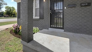 A modern building with a brick facade, a black metal gate, and a concrete porch. - Stylish Memphis Home w/ Large Yard + Cozy Interior (Memphis)