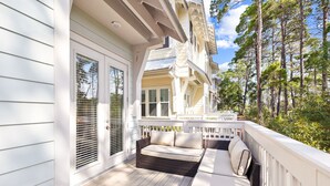 A covered porch with a wicker sofa and a table, overlooking a forested area. - New 30A Listing! Remodeled Home + New Golf Cart (Inlet Beach)