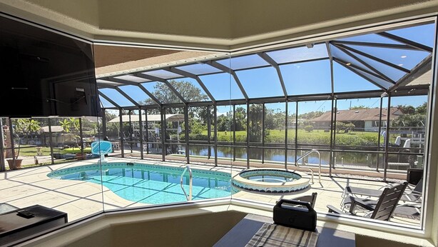 Quarto de canto com uma grande janela com vista para uma área de piscina, televisão na parede e uma mesa com controle remoto e objetos decorativos.