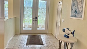 Um hall de entrada com uma porta dupla, uma pequena mesa com uma escultura de peixe e um mapa na parede.