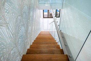 Un escalier moderne avec des marches en bois et des rampes en verre, menant à un espace intérieur lumineux.