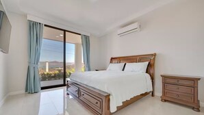 Ein Schlafzimmer mit einem großen Bett, einem Nachttisch, einer Schiebetür zu einem Balkon und einer Wand-Klimaanlage.