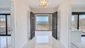 Ein Flur mit Blick auf einen Balkon, einer modernen Leuchte und einer Tür zu einem Zimmer.