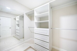 Un dressing avec des étagères et des tiroirs ouverts, une porte et un miroir.