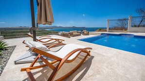Ein Poolbereich mit Liegestühlen und Blick auf das Meer.