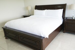 A large, dark wood bed with white linens, two bedside tables with lamps, and a drawer unit under the bed. - Flamingo Next to the Beach Villa Mauka (Playa Flamingo)