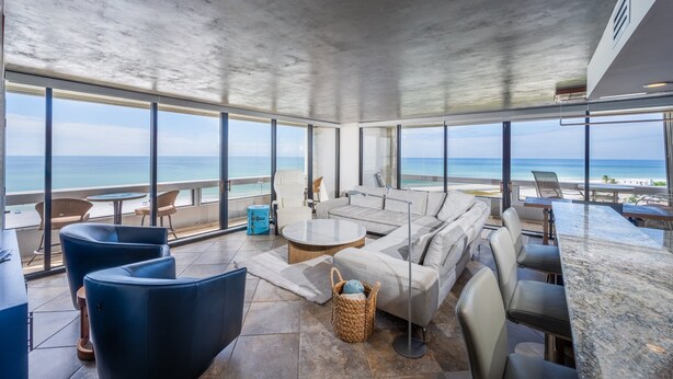 Un área de descanso moderna con un amplio ventanal con vista a la playa, amueblada con sofás, sillones y una barra.