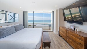 Un dormitorio con una cama grande, un aparador de madera, un banco y un televisor montado en la pared.