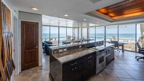 Una cocina moderna con una isla grande, un comedor con vista al océano y una sala de estar amplia con un gran ventanal con vista al mar.