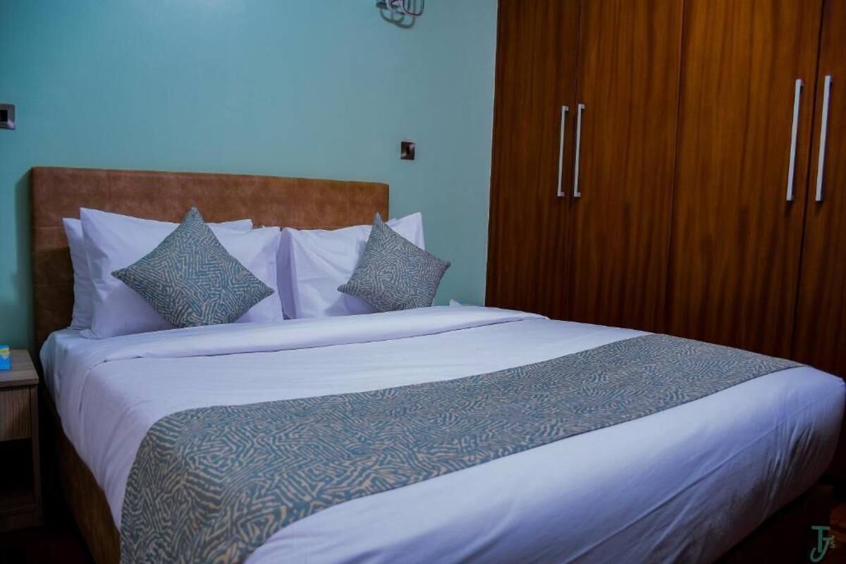 A neatly made bed with patterned bedding, a wooden headboard, and a wardrobe with two doors.