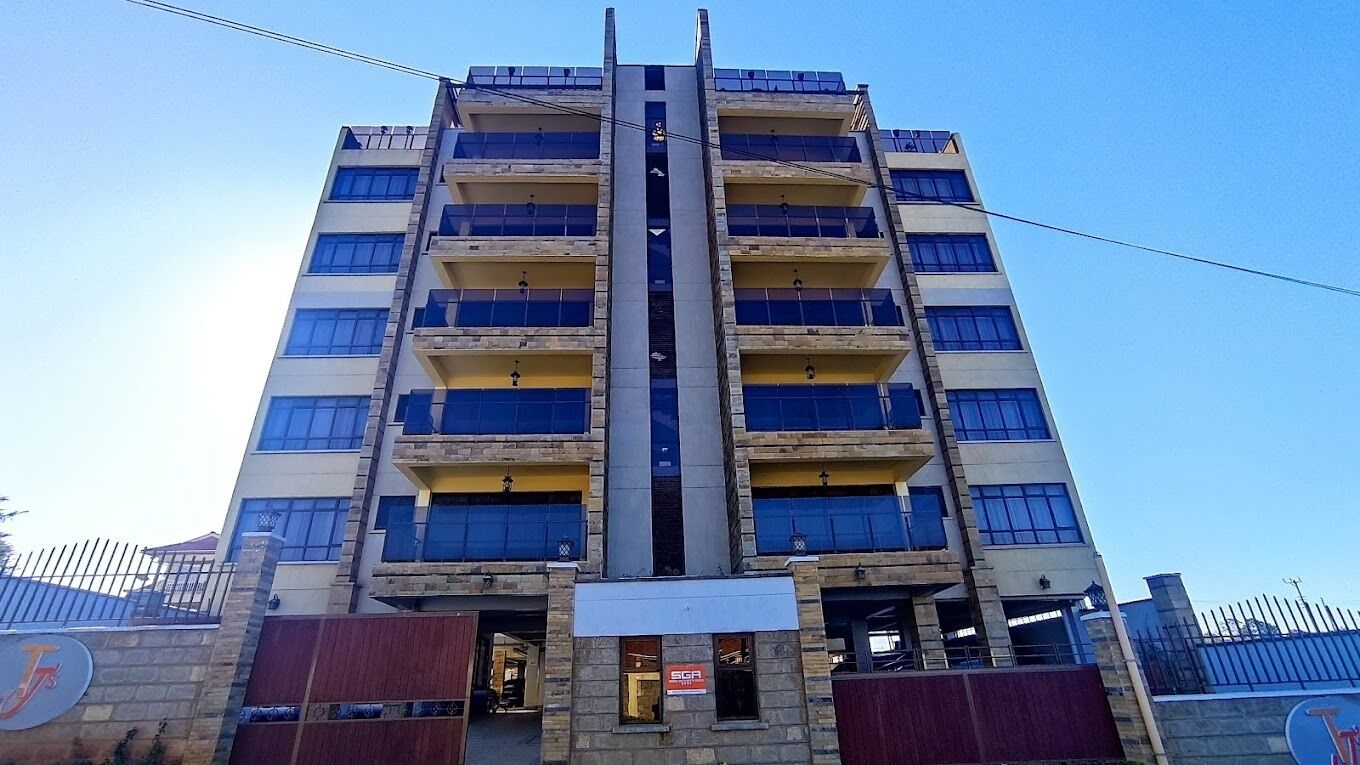 A multi-story building with a central vertical structure, balconies on each floor, and a visible entrance with a sign.