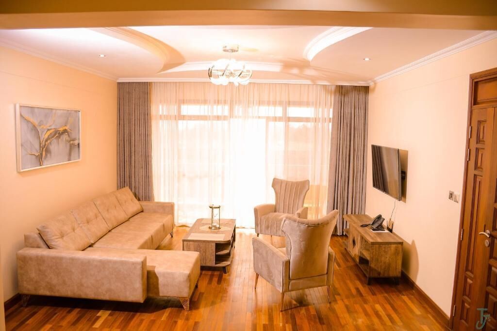 A living room with a sofa, armchairs, a coffee table, a TV, and a door.
